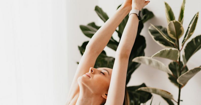 Active Lifestyles - From above sporty calm female in gray sports bra performing Upward Salute exercise while practicing yoga in light living room