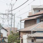 Cycling Infrastructure - Unrecognizable person wearing hat riding bicycle over railway crossing equipped with semaphore in downtown of Japan city