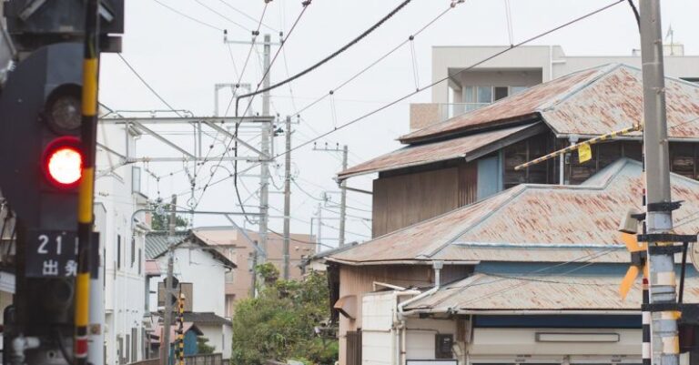 Cycling Infrastructure - Unrecognizable person wearing hat riding bicycle over railway crossing equipped with semaphore in downtown of Japan city