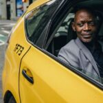 Transport Use - Happy confident mature African American male looking away and expecting important message on mobile phone while sitting in yellow automobile