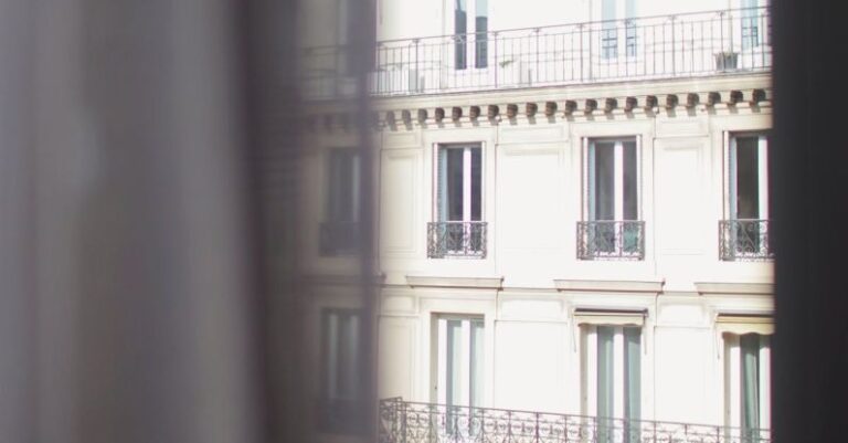 Urban Housing - Hotel with elegant balconies and bay windows in Paris as seen from opposite building through slightly ajar window curtains on sunny day