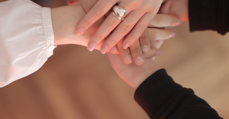 Community Engagement - Top view of faceless friends in different clothes stacking hands together while standing on wooden floor indoor on sunny day